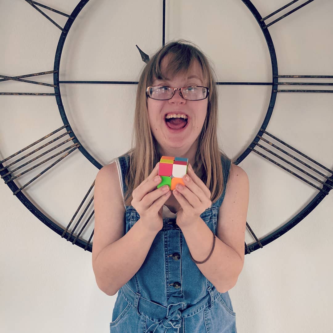 Katie scrambling a Rubik's cube in front of a clock